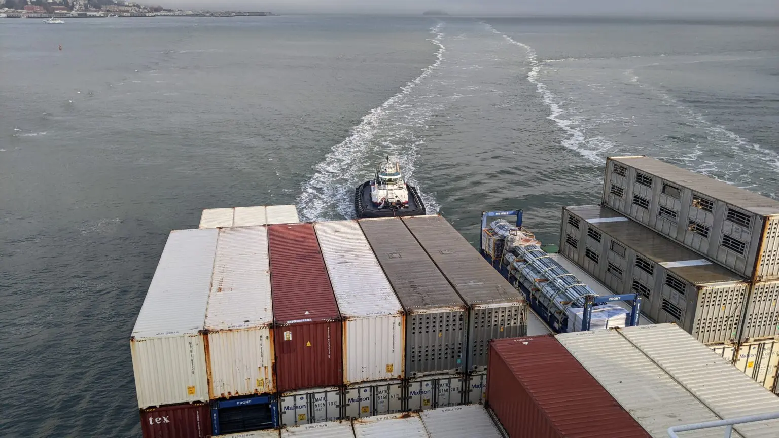 A boat is traveling down the water near some cargo containers.
