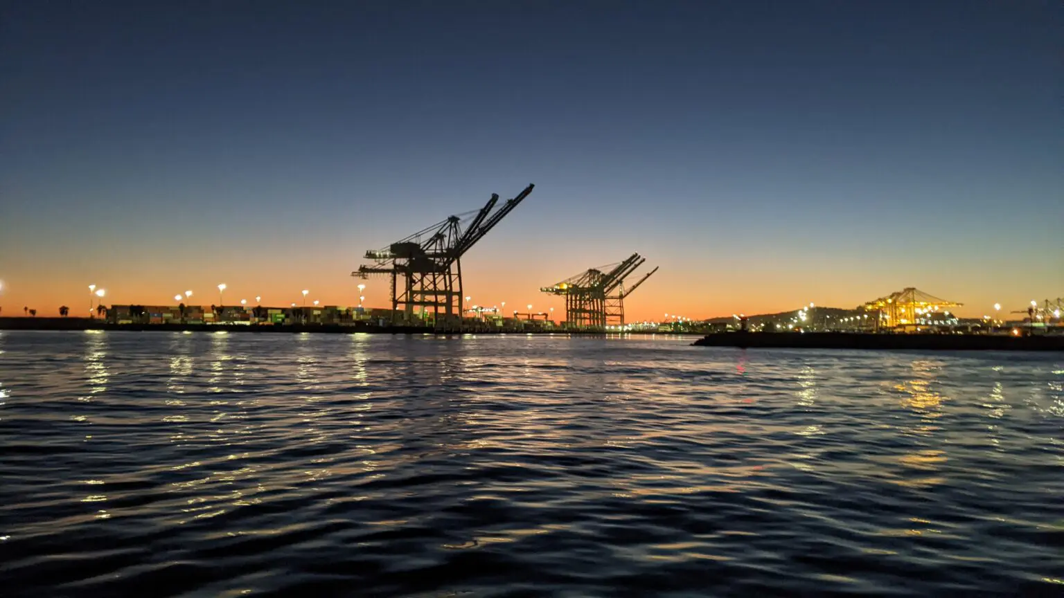 A view of the ocean at dusk with cranes in the background.