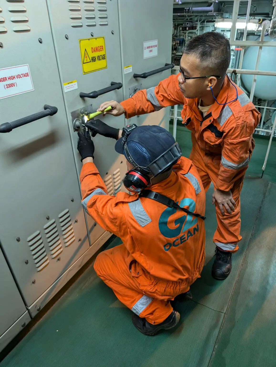 Two men in orange work suits are fixing a cabinet.